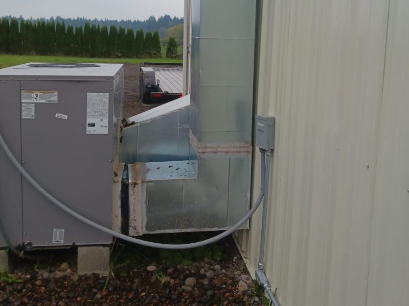New galvanized supply duct connecting a packaged HVAC unit through a metal building wall
